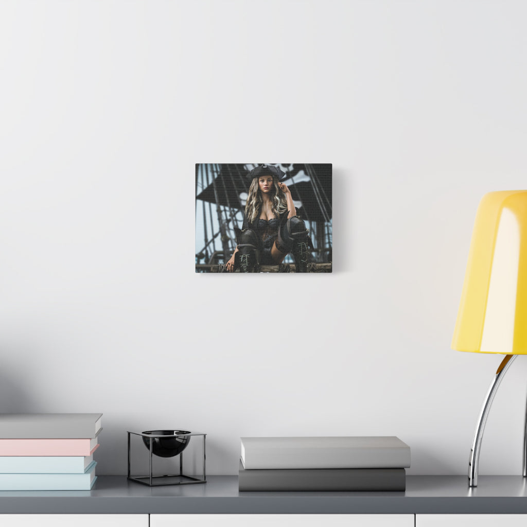 A framed wall art print depicting a woman on a ship's deck, displayed on a white wall above a gray console table with books, a small black bowl in a wire frame, and a yellow lamp.