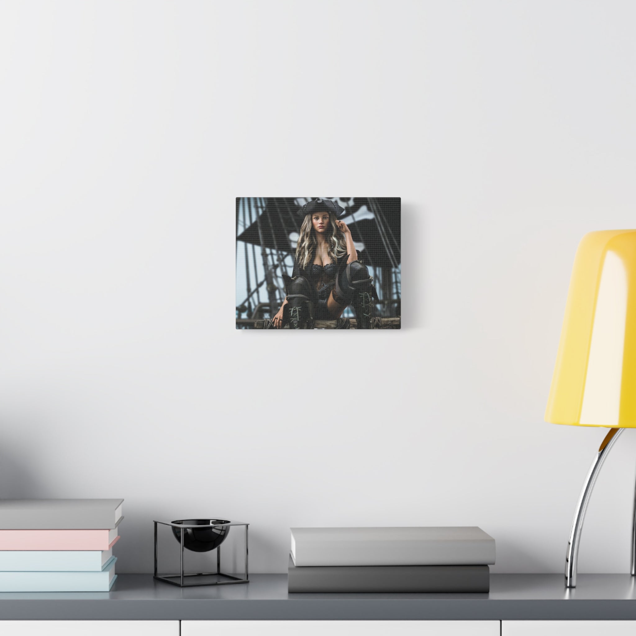 A framed wall art print depicting a woman on a ship's deck, displayed on a white wall above a gray console table with books, a small black bowl in a wire frame, and a yellow lamp.